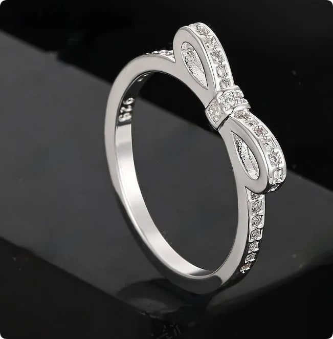 Silver colour bow-shaped ring with rhinestone and zircon crystal decoration on a finger.
