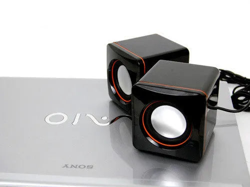 Small black square USB computer speaker on a desk next to a laptop.