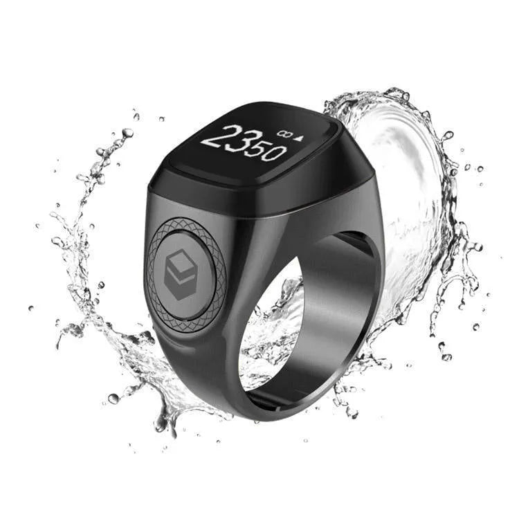 Zikr1 smart ring in silver on a charging cable next to its case, showing the OLED display.