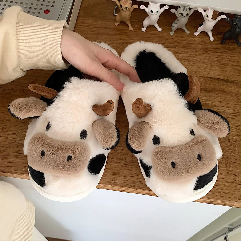 White cow-patterned plush slippers for women with a non-slip textured sole on a wooden floor