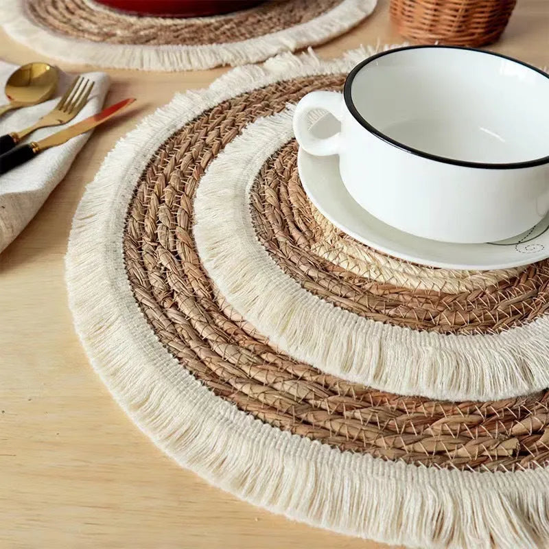 A round natural papyrus straw placemat with decorative tassels, shown in a solid colour.