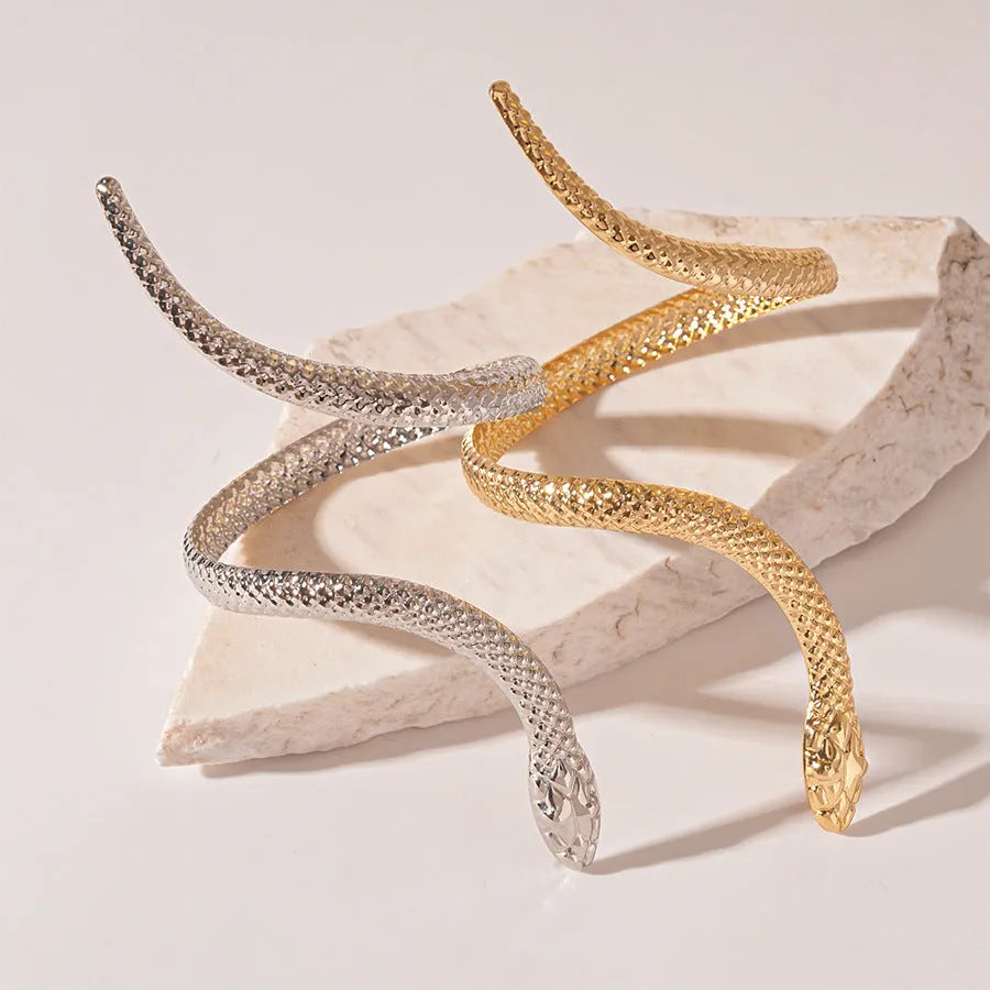 Gold twisted snake design metal bracelet and ring set on a white background.