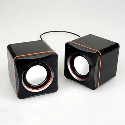 Small black square USB computer speaker on a desk next to a laptop.