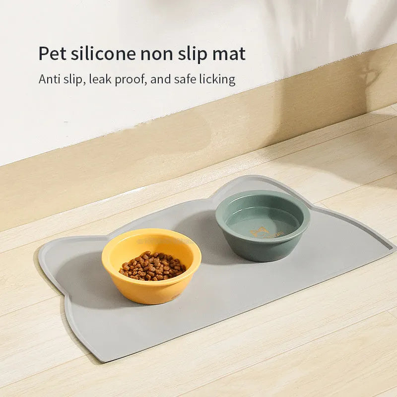 Blue silicone pet feeding mat with cat head shape under food and water bowls.