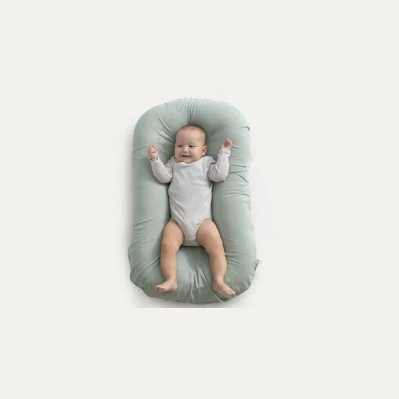 Beige portable cotton baby nest crib for newborn infants on a bed.
