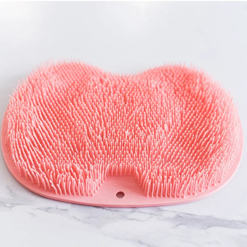 Orange silicone bath massage brush with suction cups on a bathroom tile floor.