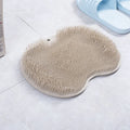 Orange silicone bath massage brush with suction cups on a bathroom tile floor.