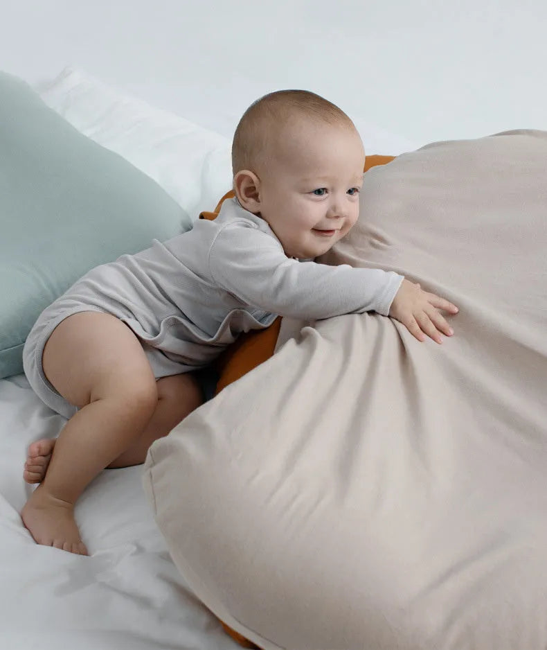 Beige portable cotton baby nest crib for newborn infants on a bed.