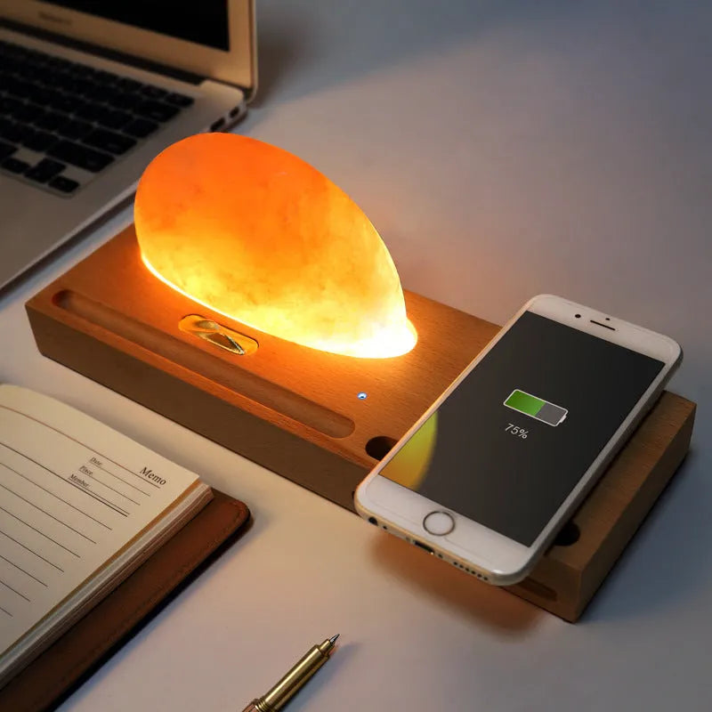 Natural crystal salt lamp with wireless charging pad on a light beech wood table base.