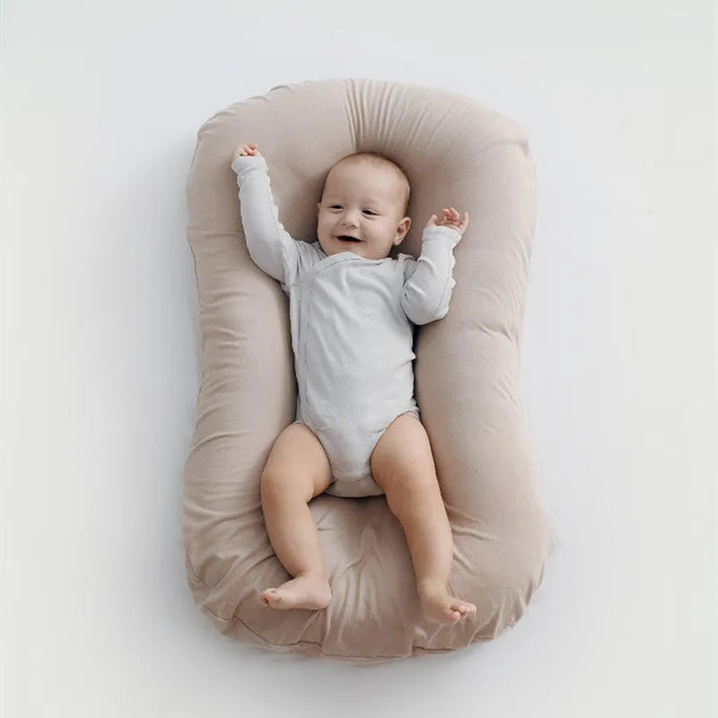 Beige portable cotton baby nest crib for newborn infants on a bed.