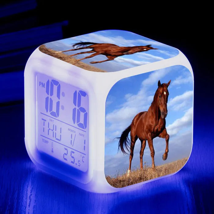 Square cartoon digital alarm clock with colour changing LED display on a plastic and plexiglass body.