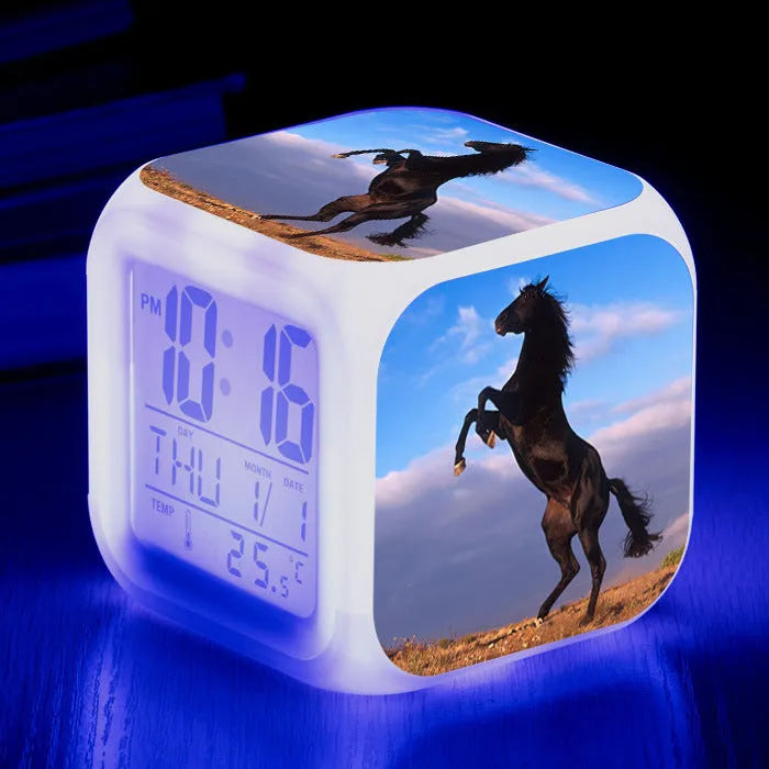 Square cartoon digital alarm clock with colour changing LED display on a plastic and plexiglass body.