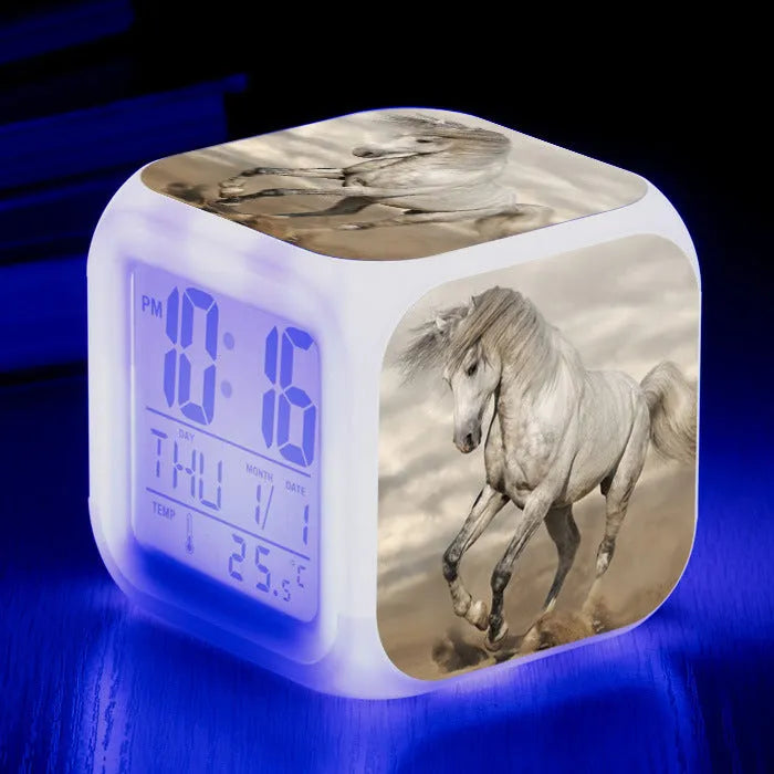 Square cartoon digital alarm clock with colour changing LED display on a plastic and plexiglass body.