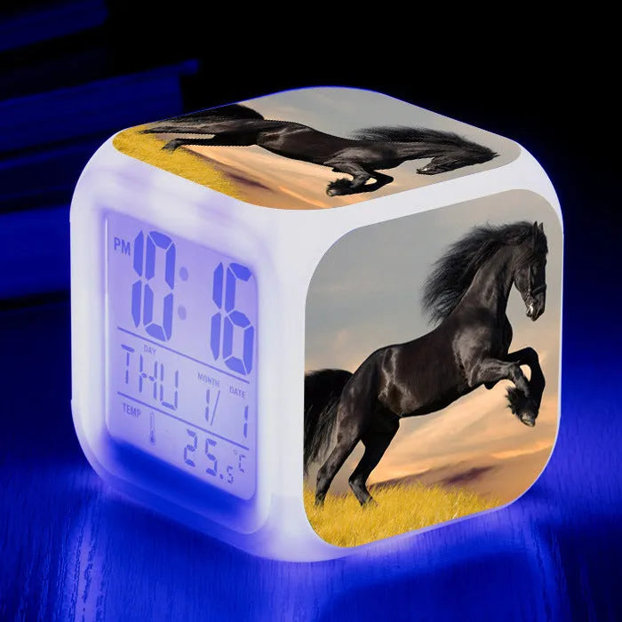Square cartoon digital alarm clock with colour changing LED display on a plastic and plexiglass body.