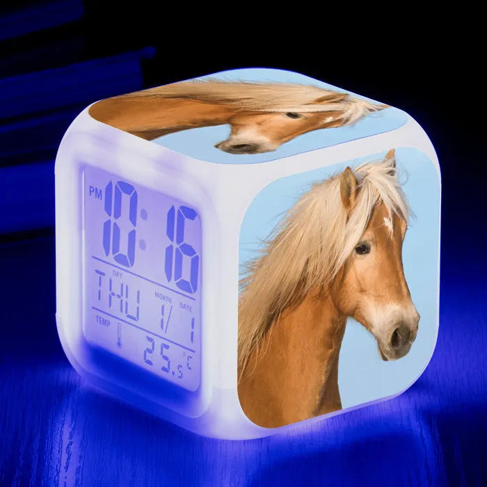 Square cartoon digital alarm clock with colour changing LED display on a plastic and plexiglass body.