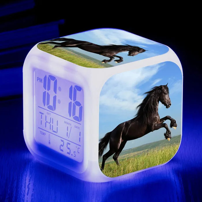 Square cartoon digital alarm clock with colour changing LED display on a plastic and plexiglass body.