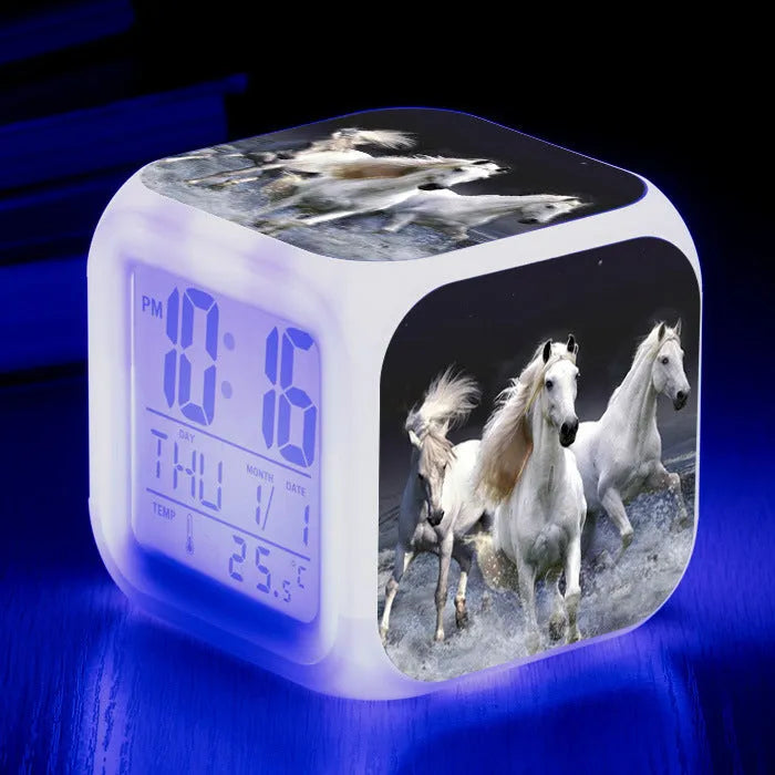 Square cartoon digital alarm clock with colour changing LED display on a plastic and plexiglass body.
