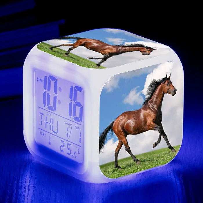 Square cartoon digital alarm clock with colour changing LED display on a plastic and plexiglass body.