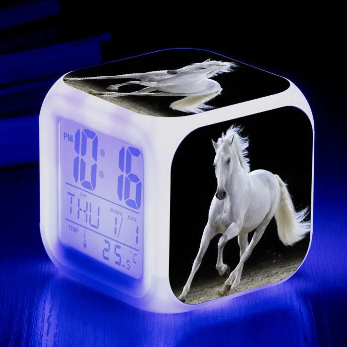 Square cartoon digital alarm clock with colour changing LED display on a plastic and plexiglass body.