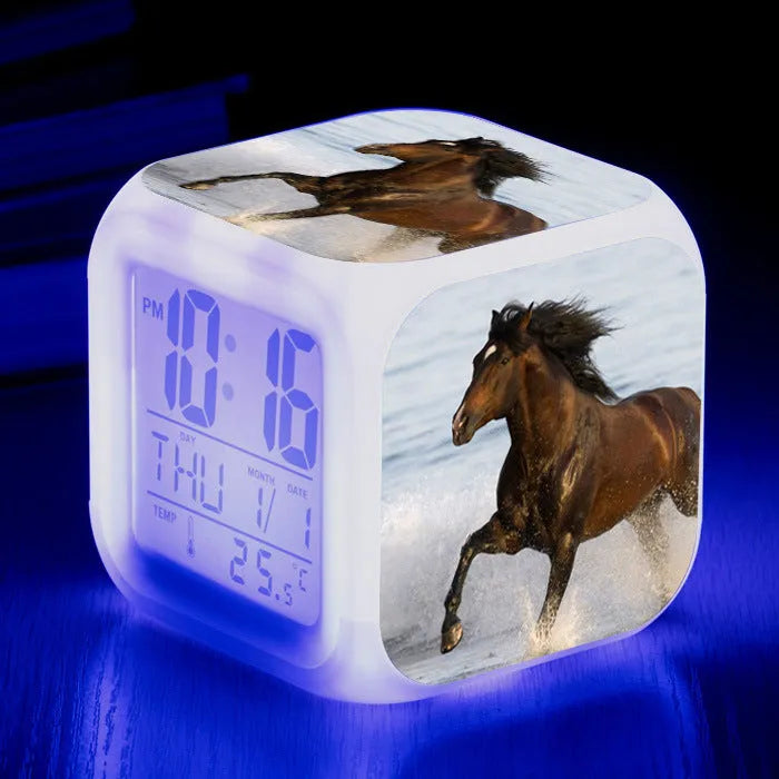 Square cartoon digital alarm clock with colour changing LED display on a plastic and plexiglass body.