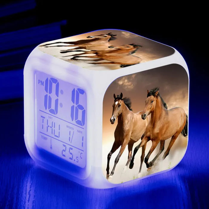 Square cartoon digital alarm clock with colour changing LED display on a plastic and plexiglass body.