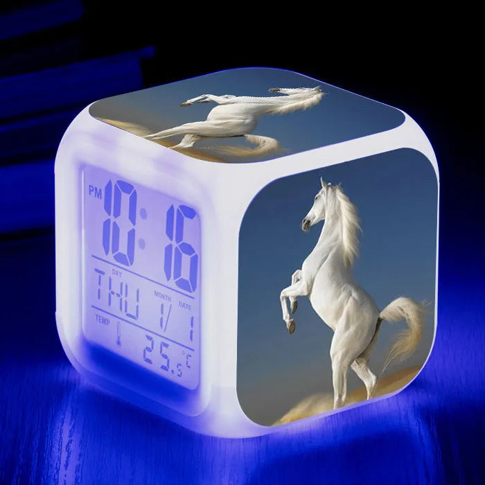 Square cartoon digital alarm clock with colour changing LED display on a plastic and plexiglass body.