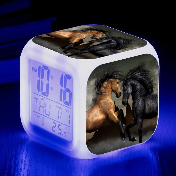 Square cartoon digital alarm clock with colour changing LED display on a plastic and plexiglass body.
