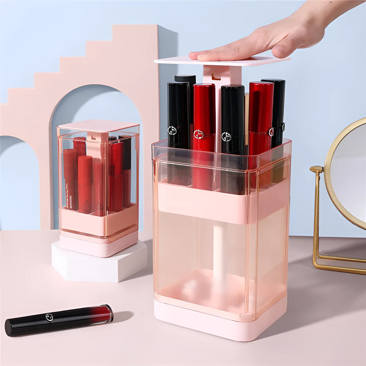 Pink press lift lipstick storage box with transparent lid on a desktop.