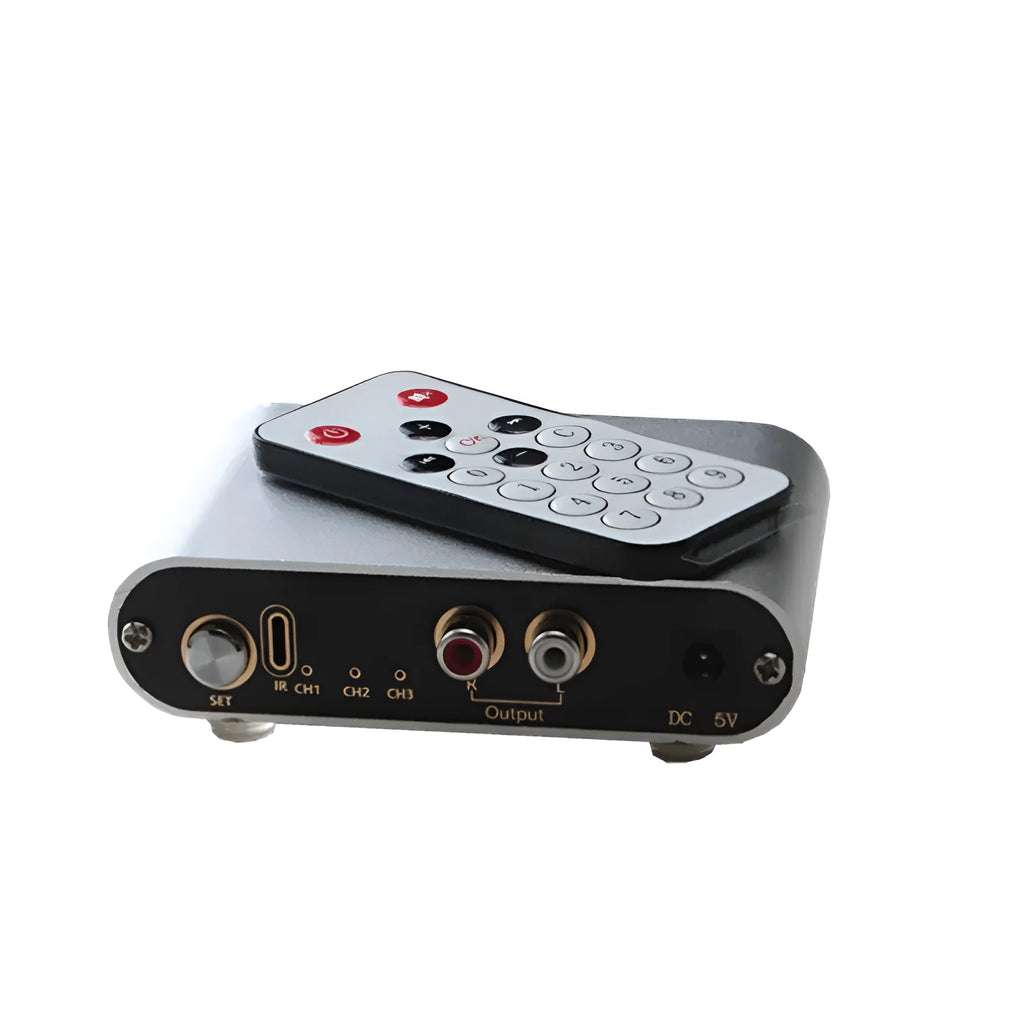 Silver aluminium audio source selector switch with infrared remote control on a shelf.