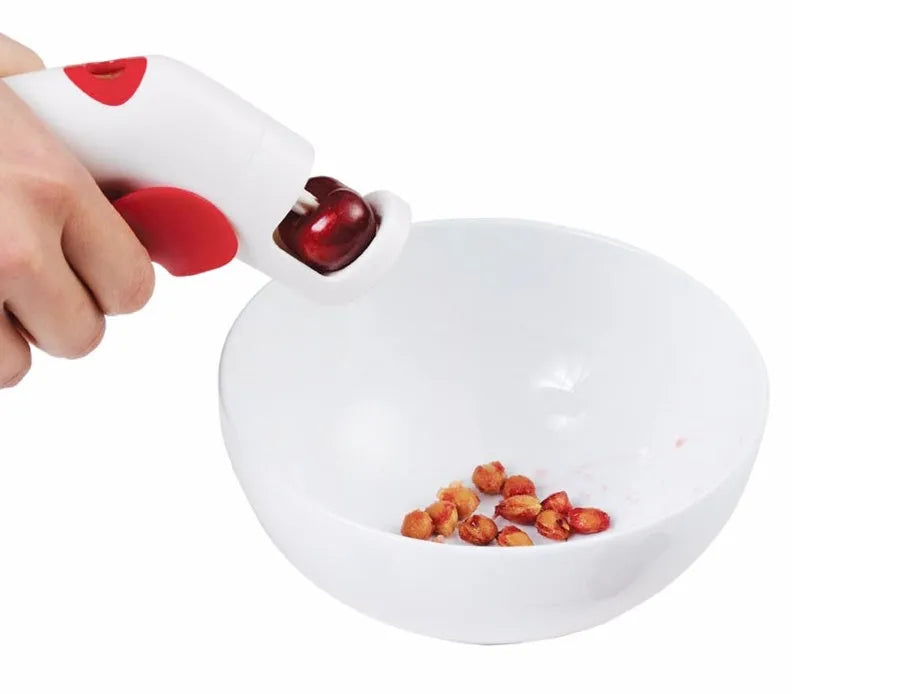Cherry stoner tool with stainless steel pitting head and white plastic handle on a wooden surface.