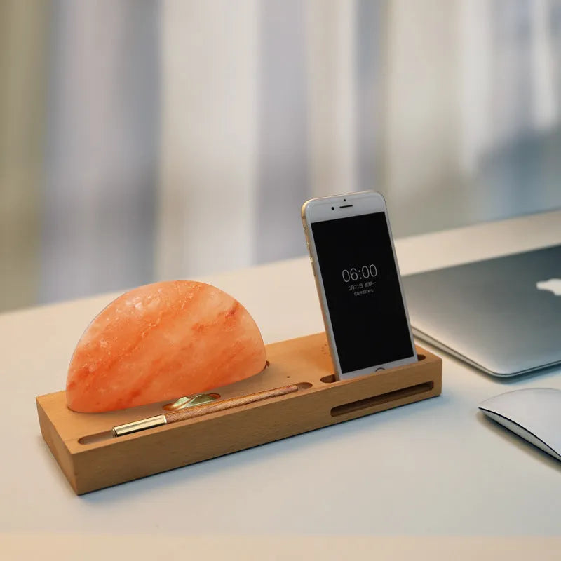 Natural crystal salt lamp with wireless charging pad on a light beech wood table base.