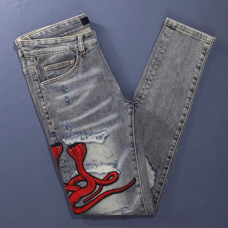 Men's slim fit jeans in old colour with distressed holes and embroidered patches on the legs.