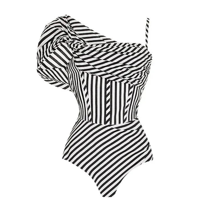 A woman wearing a ruffled striped one-piece swimsuit with a matching black skirt on a beach.