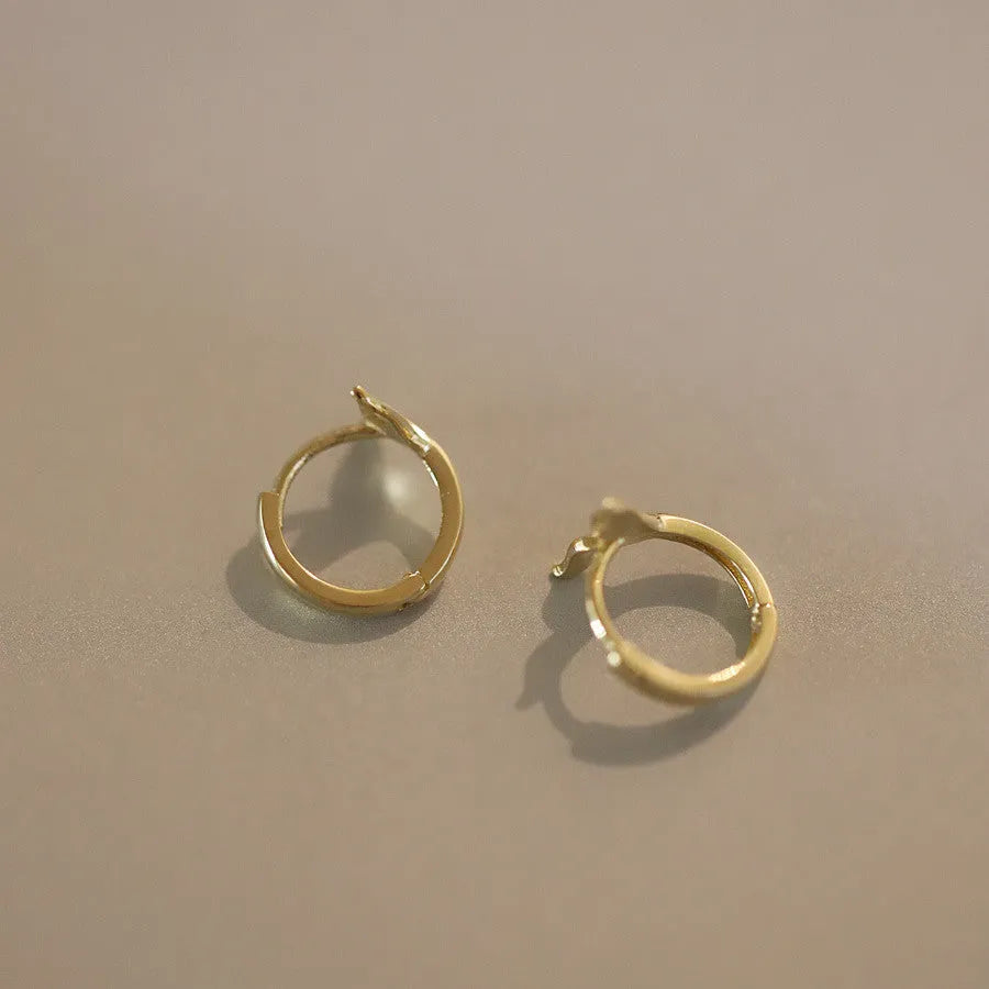 S925 sterling silver fishtail hoop earrings in gold colour on a white background.