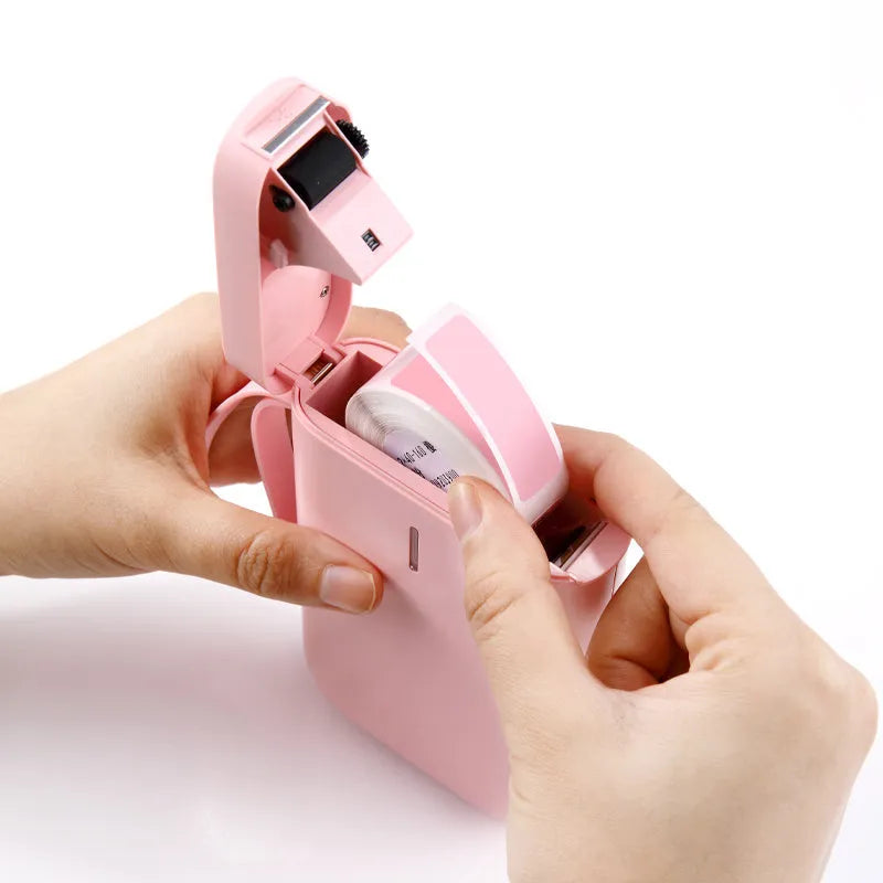 D11 compact white Bluetooth thermal label printer with USB cable and roll of label paper on a desk.