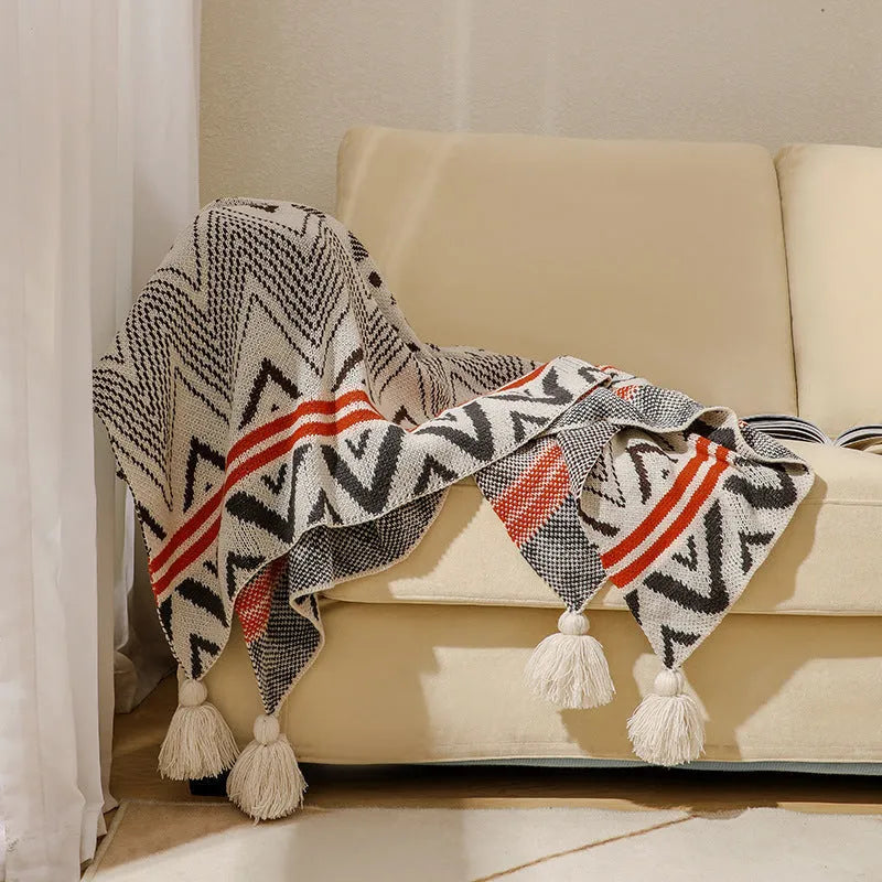 Bohemian style acrylic blanket with tassel fringe on a sofa, shown in a geometric print colour.