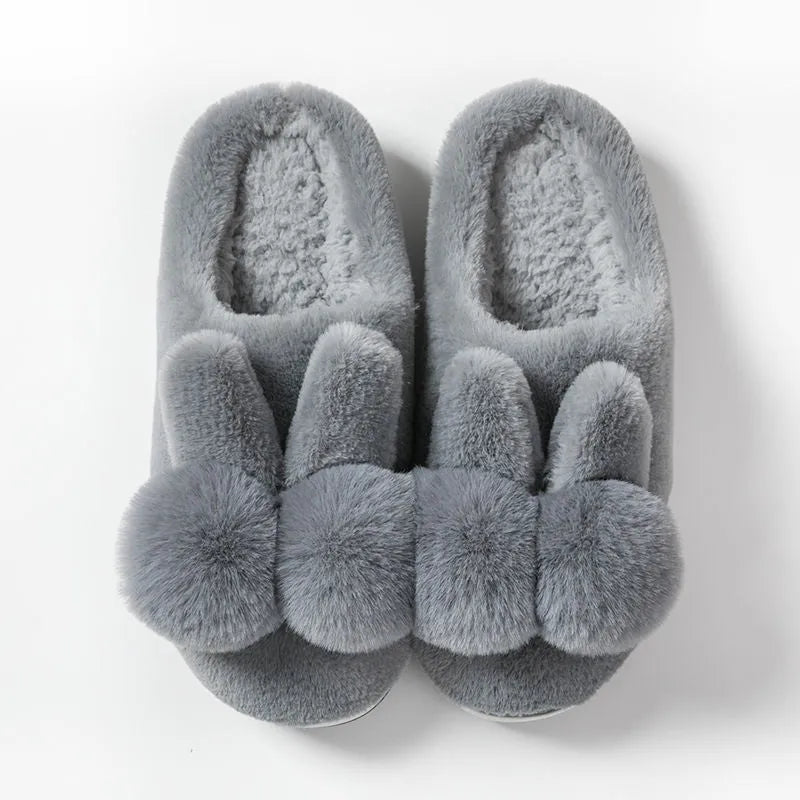 Women's fluffy bunny slippers with rabbit fur upper in cream colour on a wooden floor.