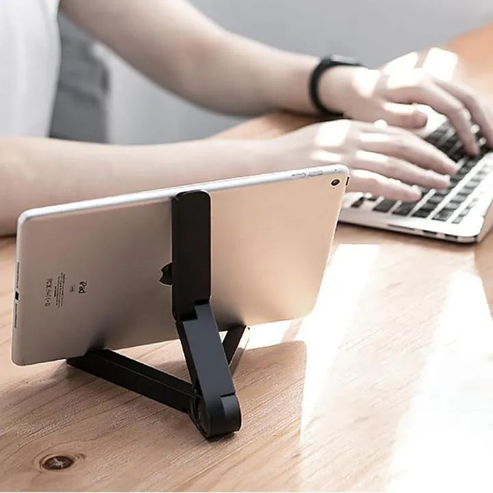 Black foldable tablet holder open on a desk supporting a tablet in landscape mode.