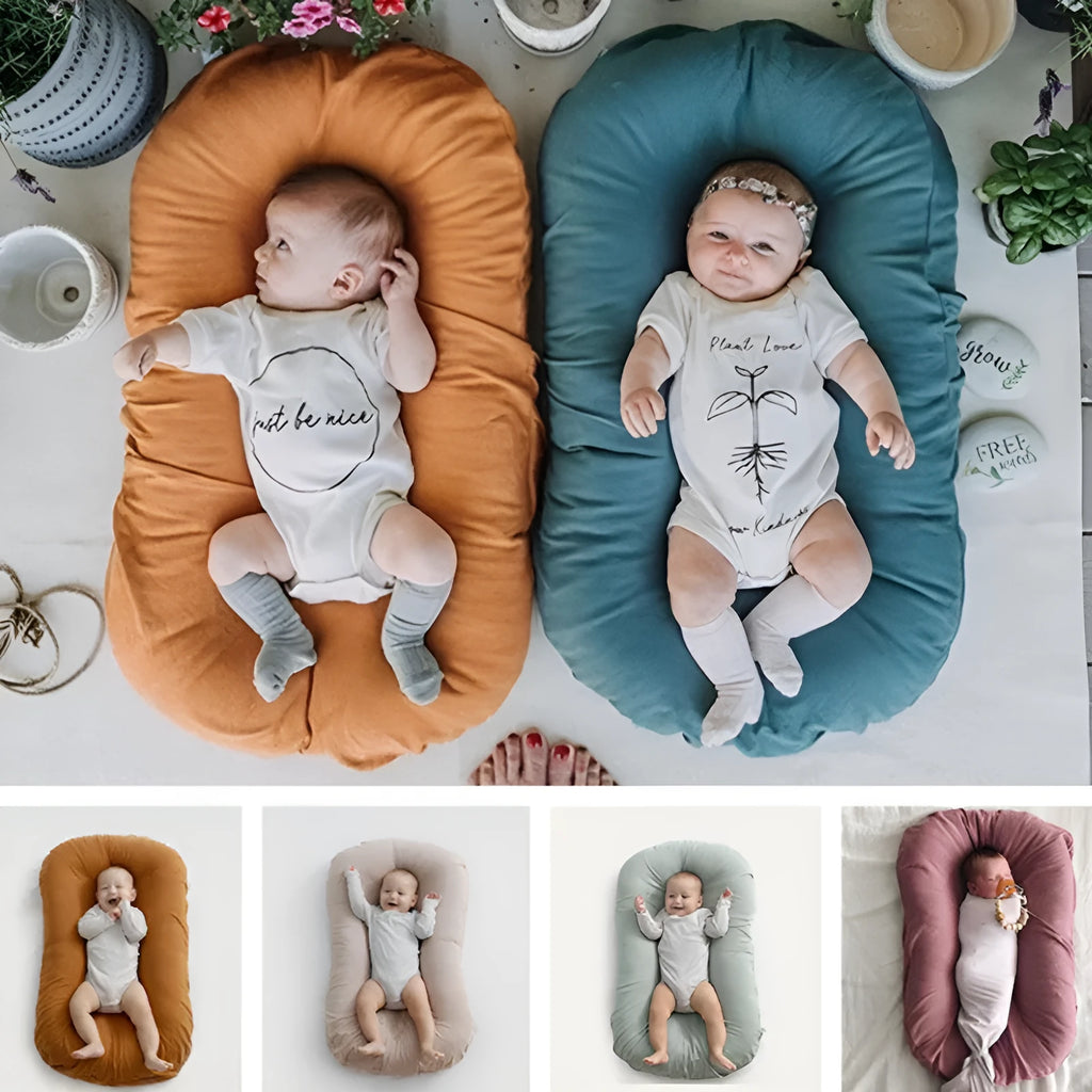 Beige portable cotton baby nest crib for newborn infants on a bed.