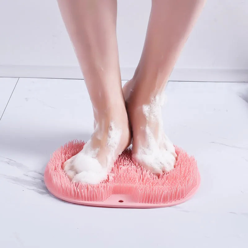 Orange silicone bath massage brush with suction cups on a bathroom tile floor.