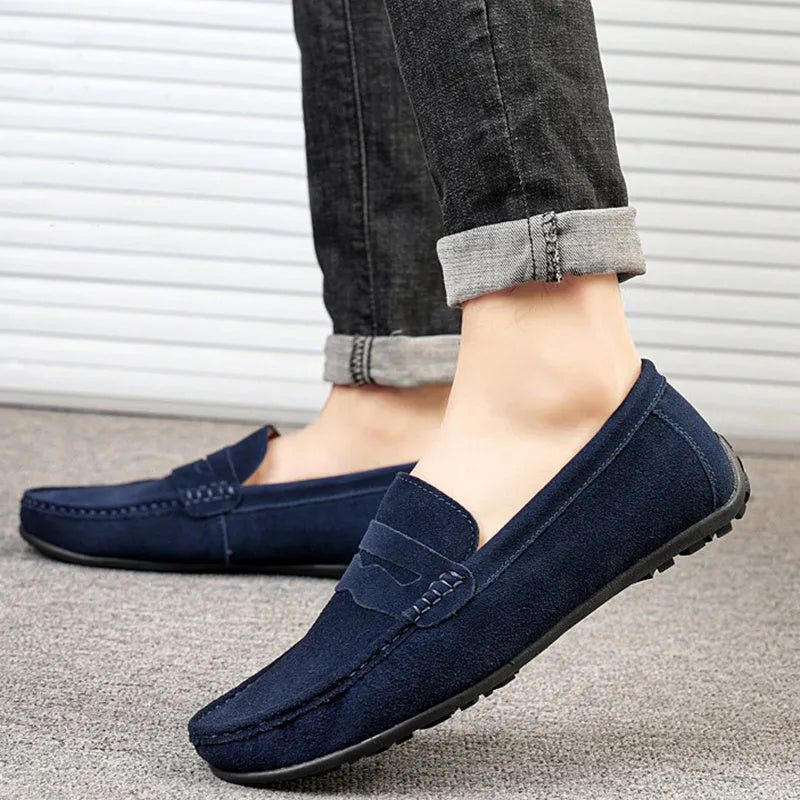 Men's solid colour suede loafers with a round toe and flat rubber sole on a neutral background.