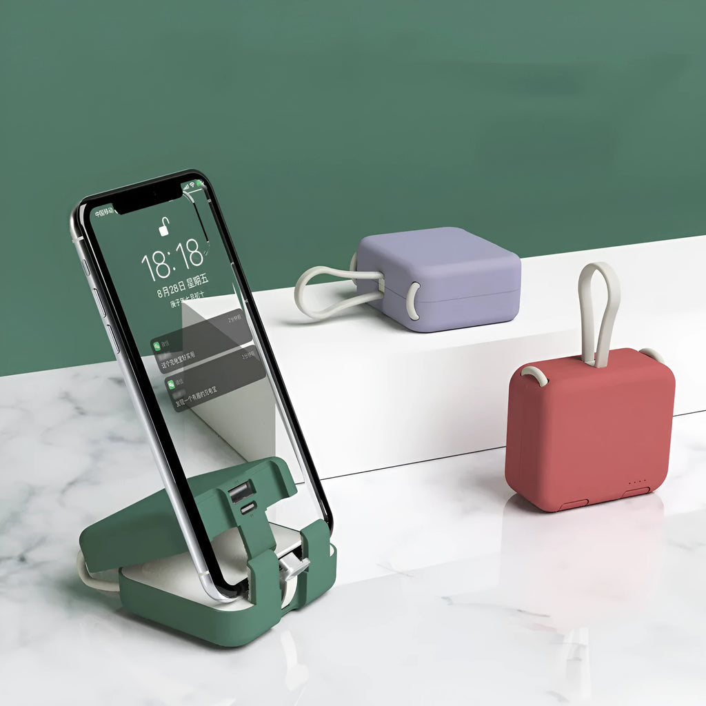 Handbag clip-on power bank in blue showing USB-A and Type-C ports, with phone propped in its integrated stand.