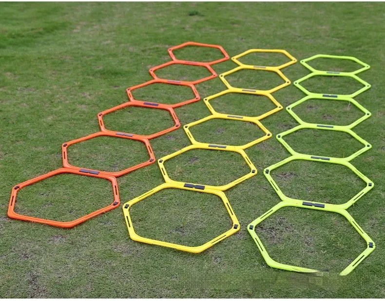 Six foldable hexagon football agility training rings in yellow, green, and orange colours laid out on grass.