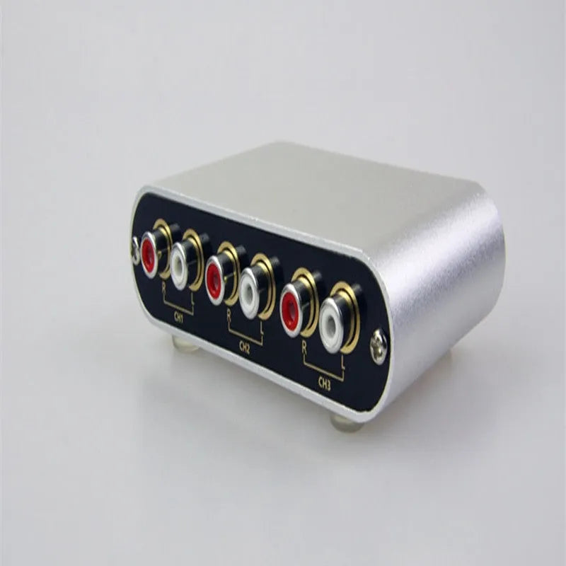 Silver aluminium audio source selector switch with infrared remote control on a shelf.