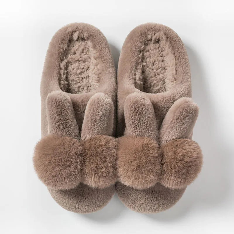 Women's fluffy bunny slippers with rabbit fur upper in cream colour on a wooden floor.