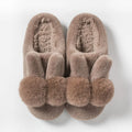 Women's fluffy bunny slippers with rabbit fur upper in cream colour on a wooden floor.
