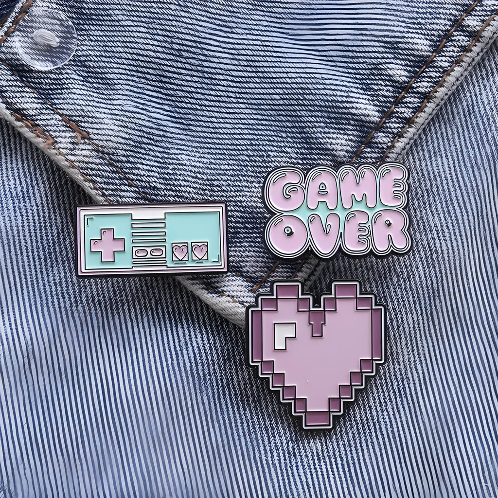 A metal alloy game console badge shown in one of three available colours, suitable for attaching to bags.
