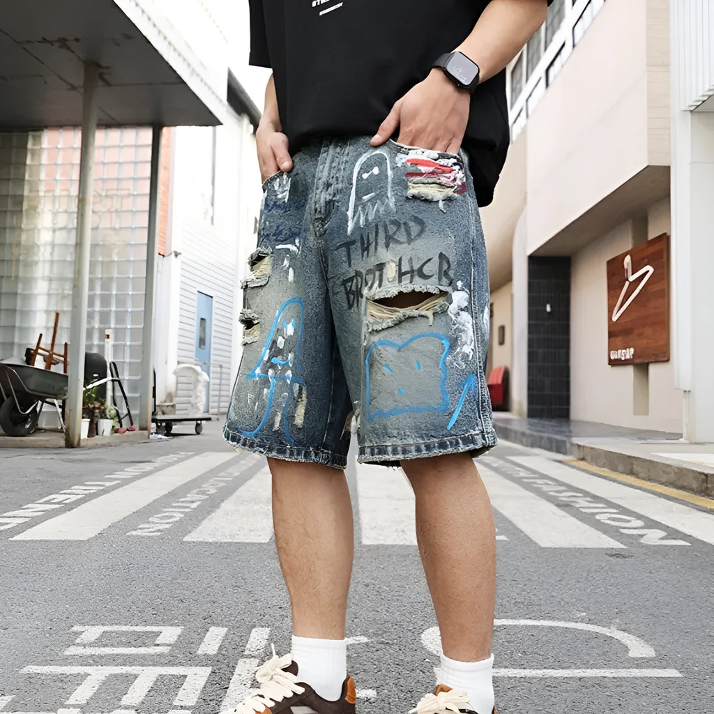 Blue ripped men's denim shorts with graffiti print and straight-leg cut.