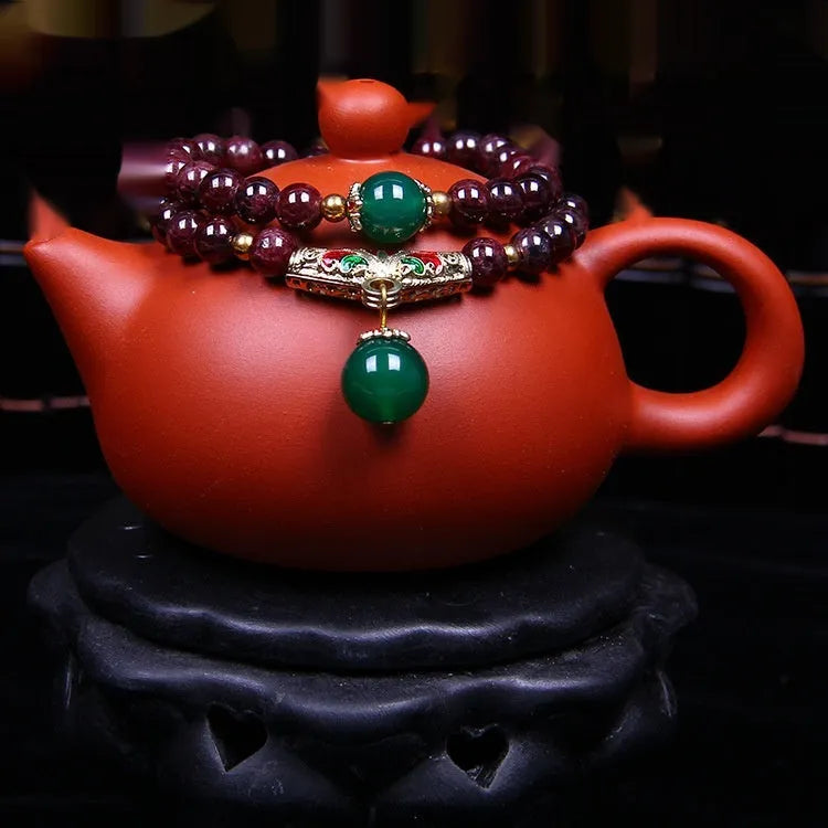 Close-up of a natural deep red garnet bead bracelet with a golden toad charm and double ring clasp.