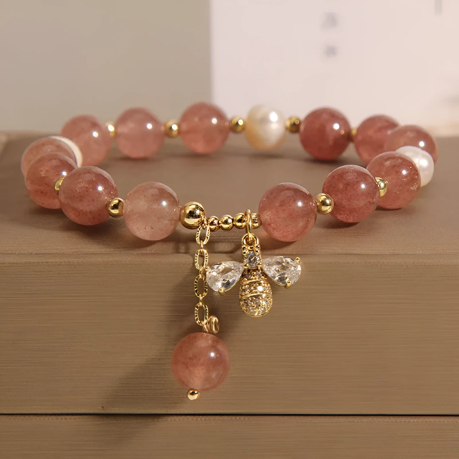 Close-up of a women's bracelet with pink strawberry quartz stones, white freshwater pearls, and sparkling zircon accents on an alloy clasp.